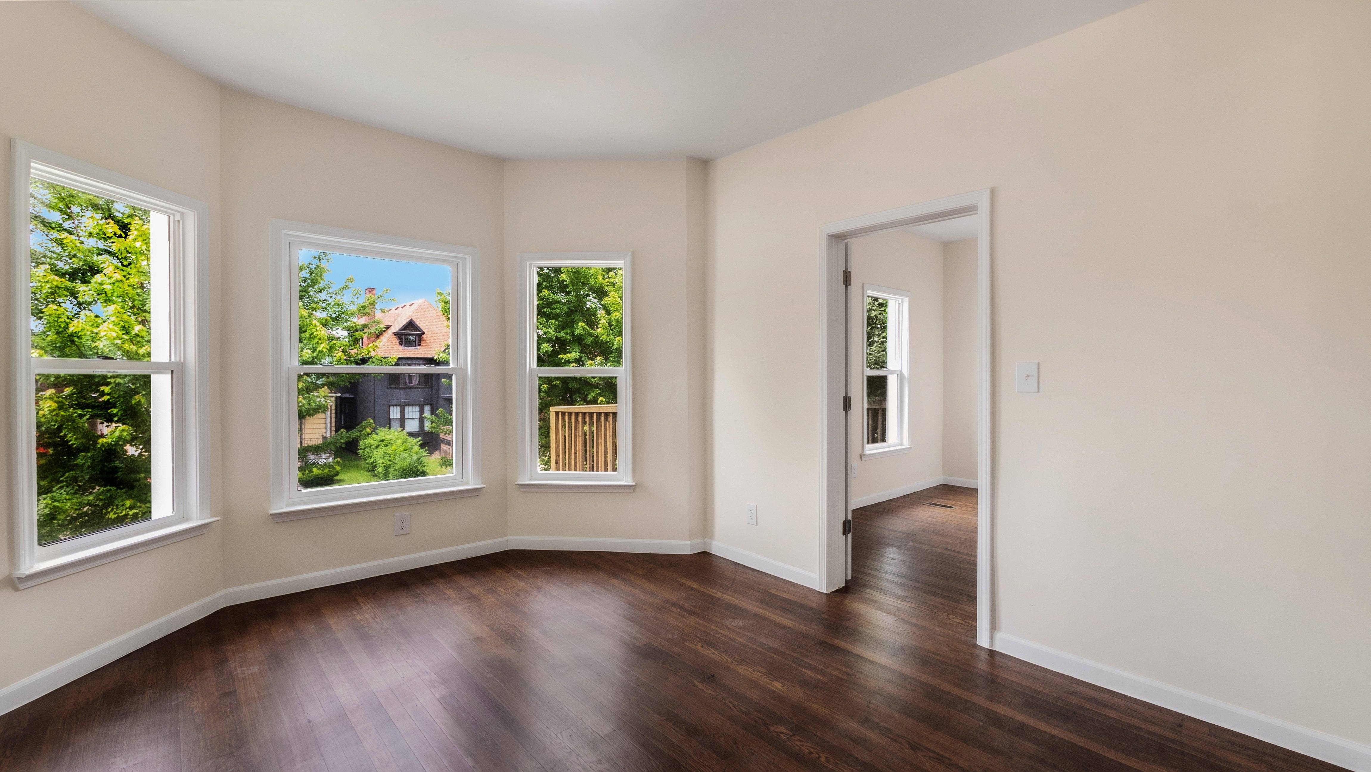 A room with a wooden floor and three windows showing the outdoors.